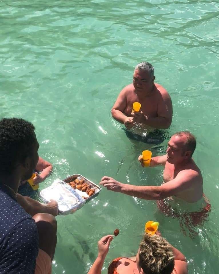 Ismaël sert accras et planteur aux passagers, dans l’eau turquoise des fonds blancs
