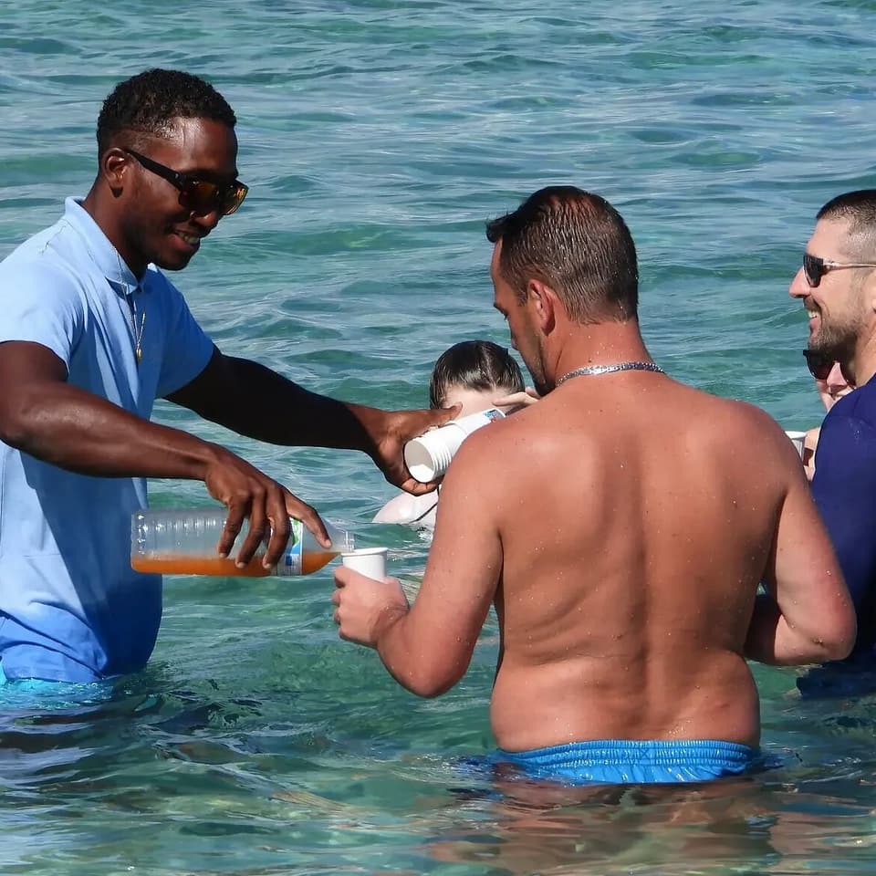 Ismaël serves homemade planter’s punch to passengers standing in the water on the sandbanks